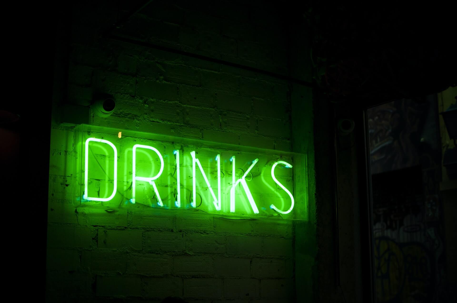 Green neon "DRINKS" sign on brick wall