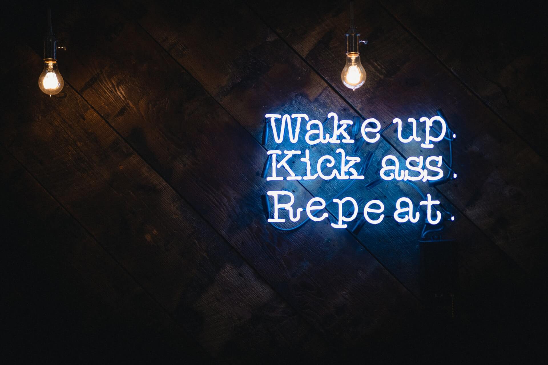 "Wake up, kick ass, repeat" neon sign on wall