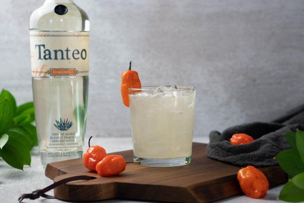 Tanteo Habanero Margarita on a board with habanero peppers with tequila bottle in background
