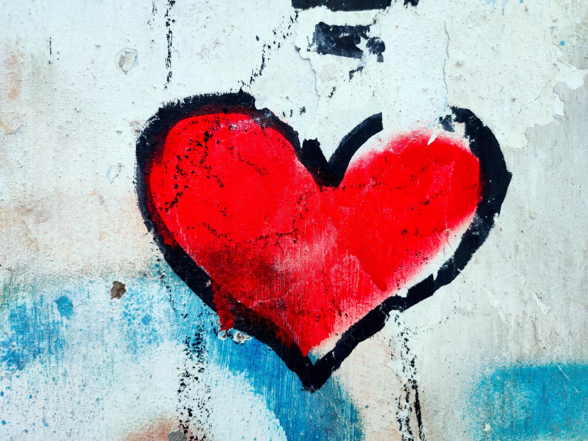 Red graffiti heart with black outline on weathered, worn wall