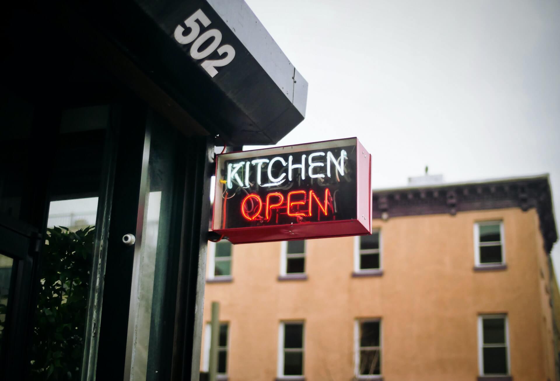 White and red neon restaurant sign that reads "Kitchen Open"