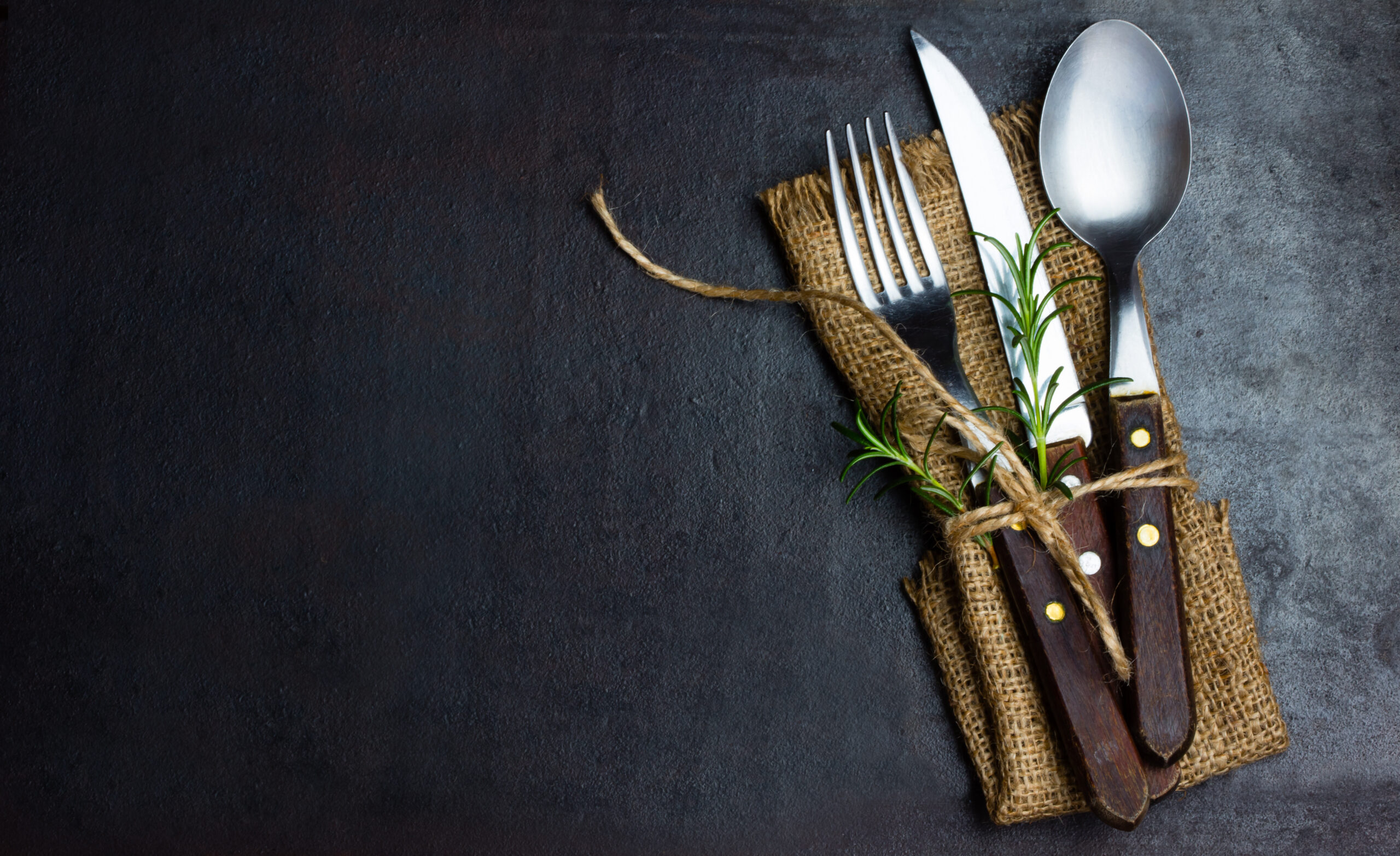 Set of fork, knife, and spoon wrapped in sustainable napkin on slate background