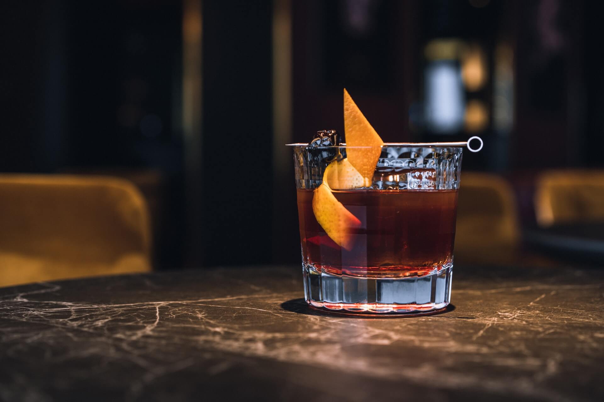 Old Fashioned cocktail garnished with orange peel and cherry on bar