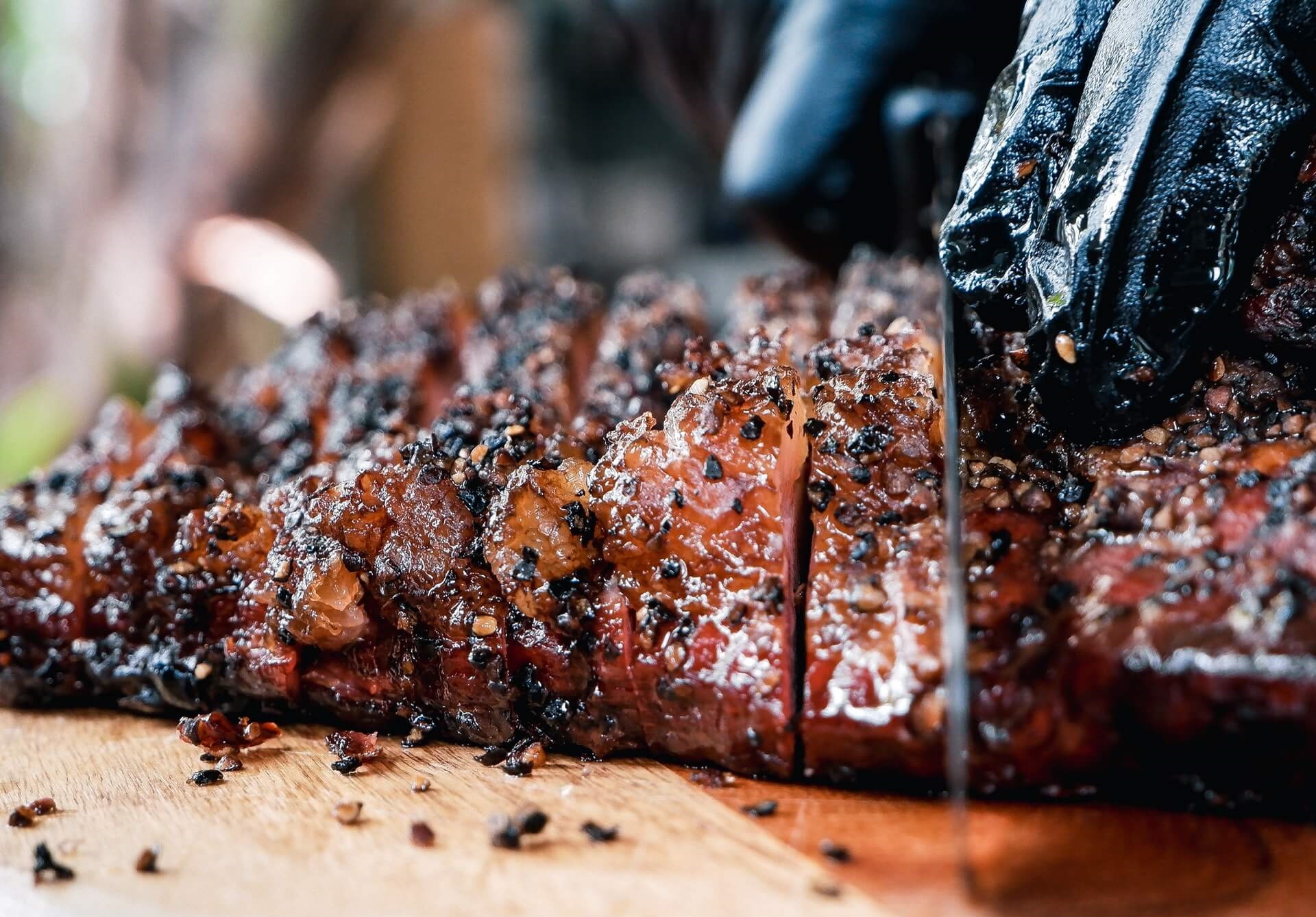 Grill master or chef slicing barbecued or grilled beef with gloved hand