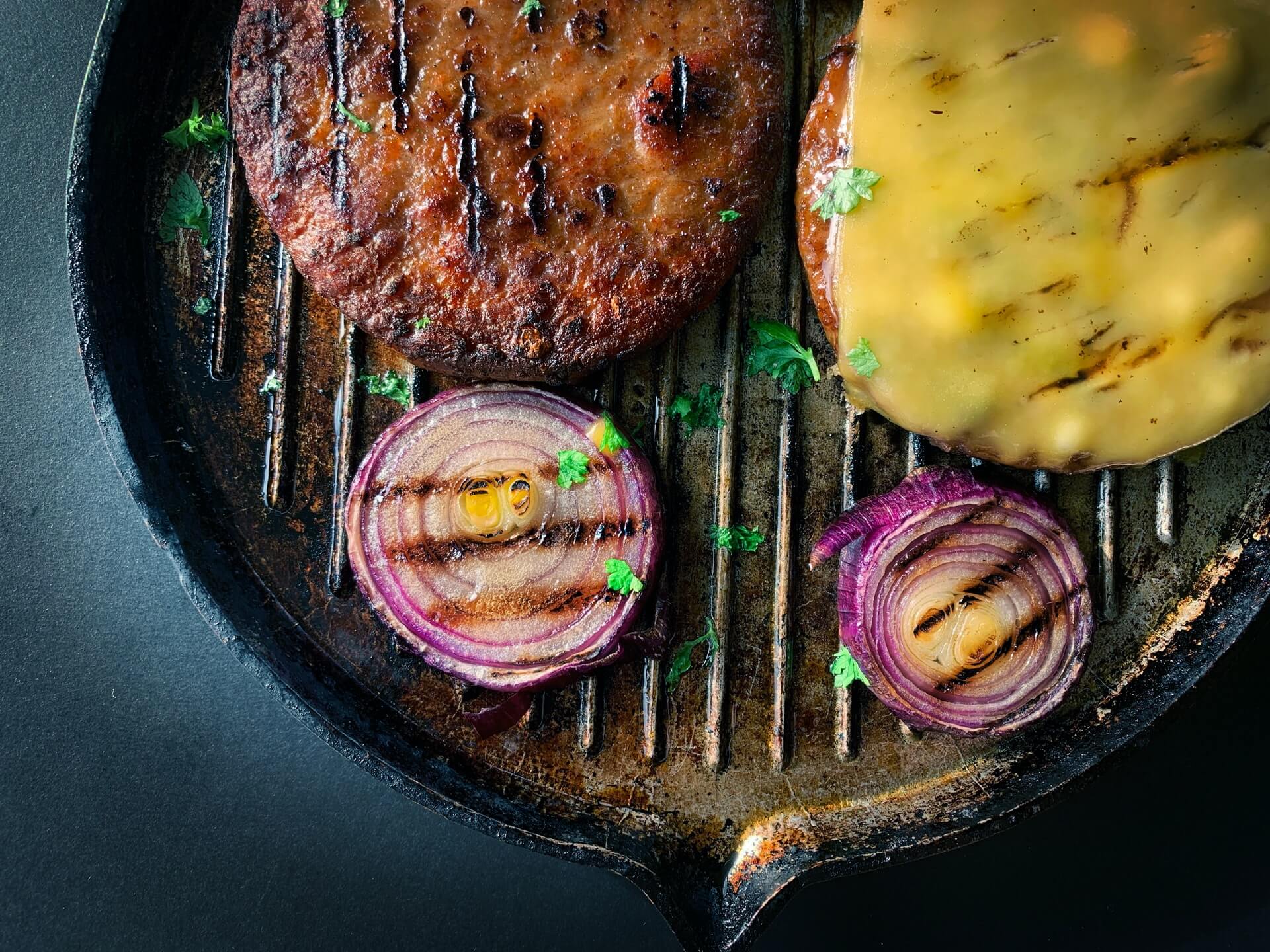 LikeMeat plant-based burgers in skillet with onions
