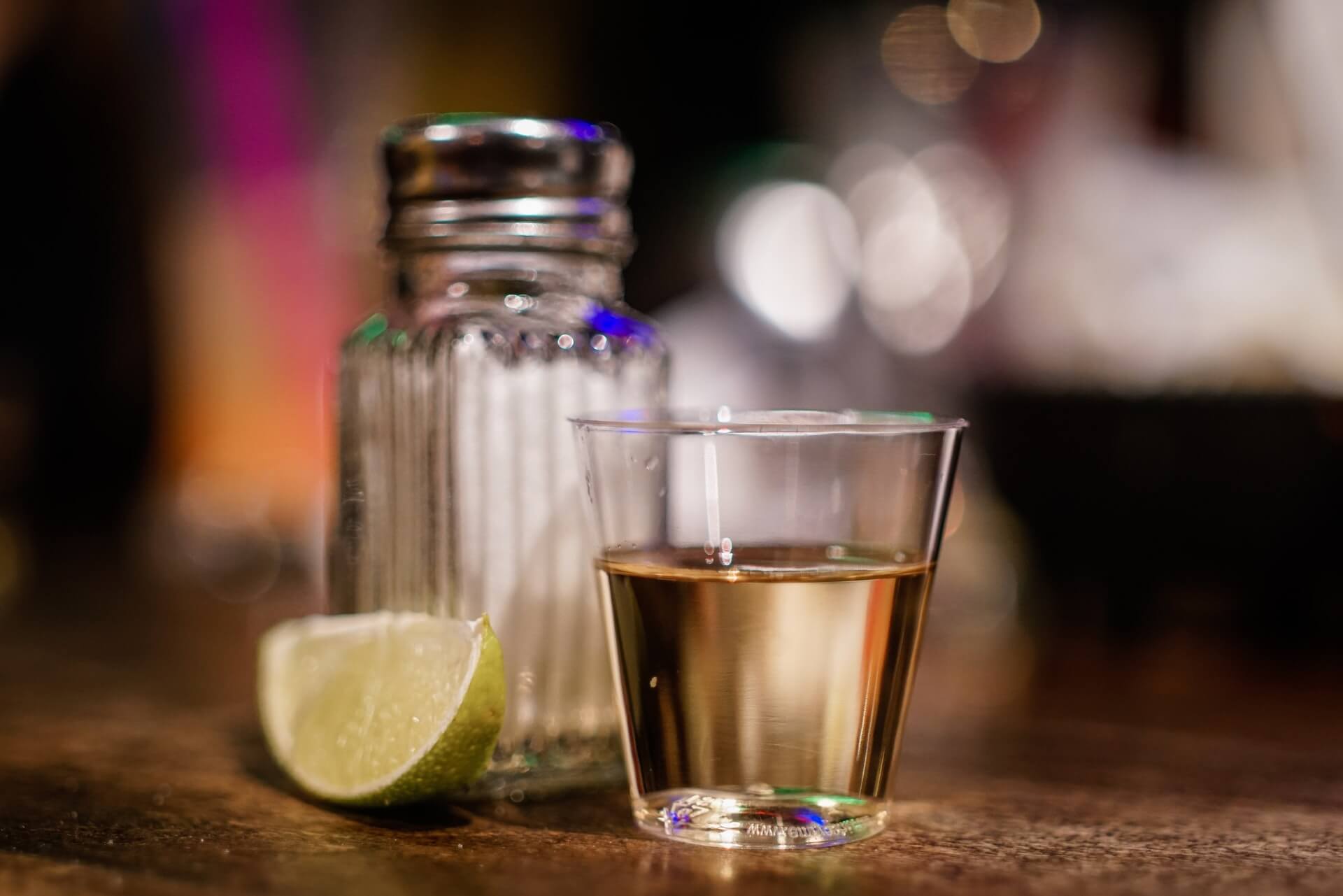 A shot of tequila served with salt shaker and lime wedge