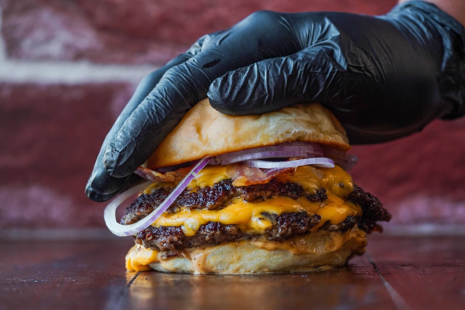 Gloved hand pressing down on cheeseburger