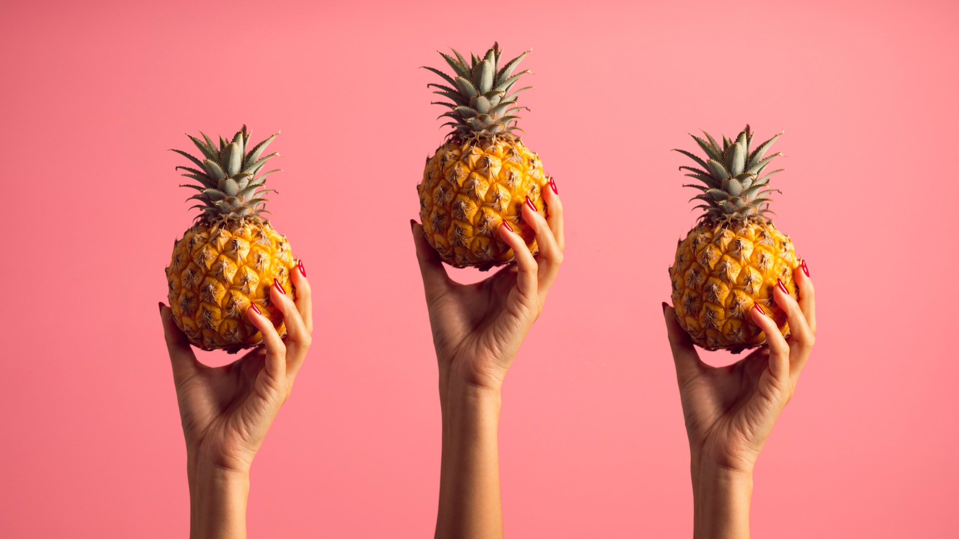 Three hands holding up three pineapples