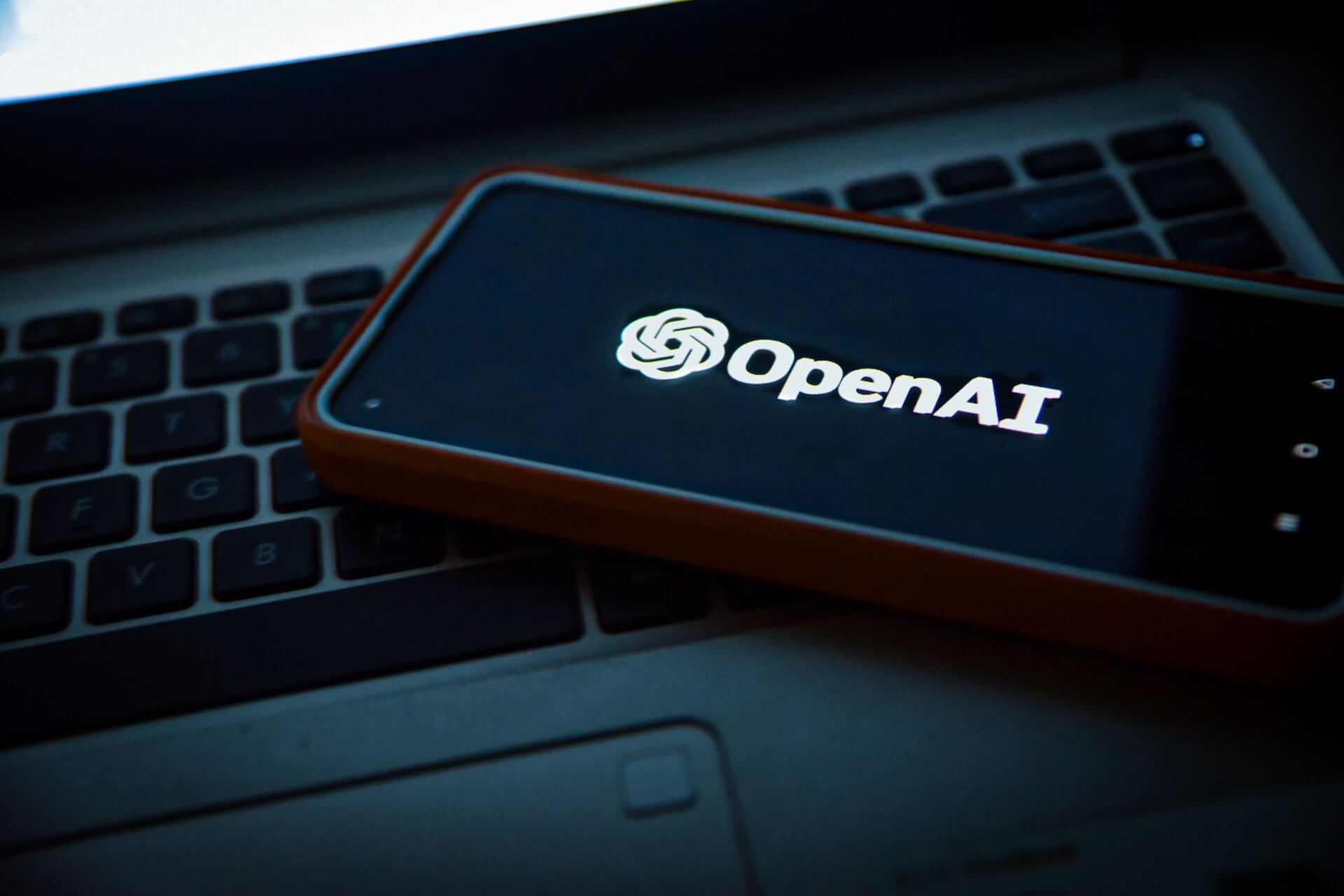 OpenAI logo on smartphone screen, resting on laptop keyboard