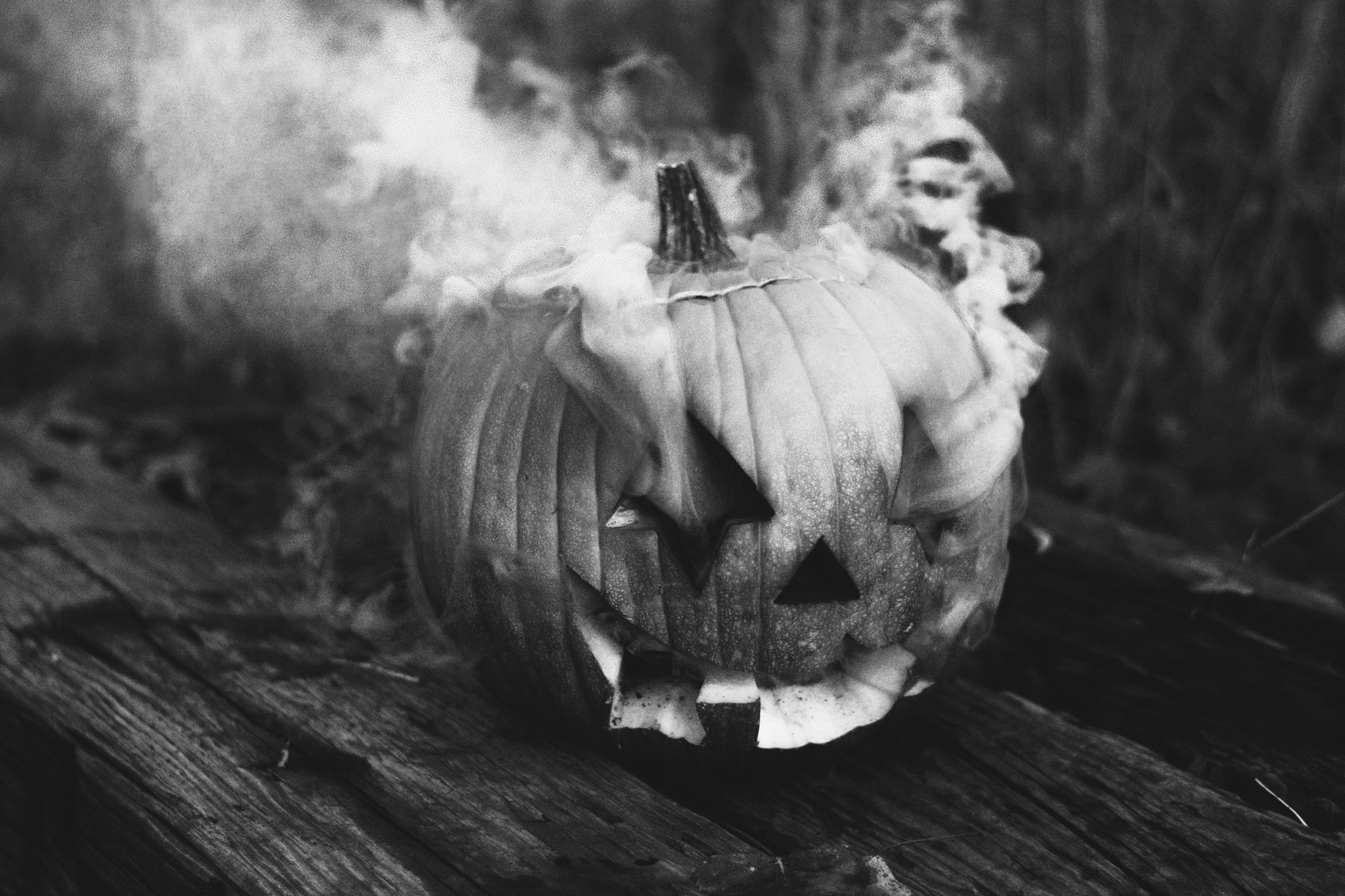 Black and white image of jack-o'-lantern with smoke coming of its eyes