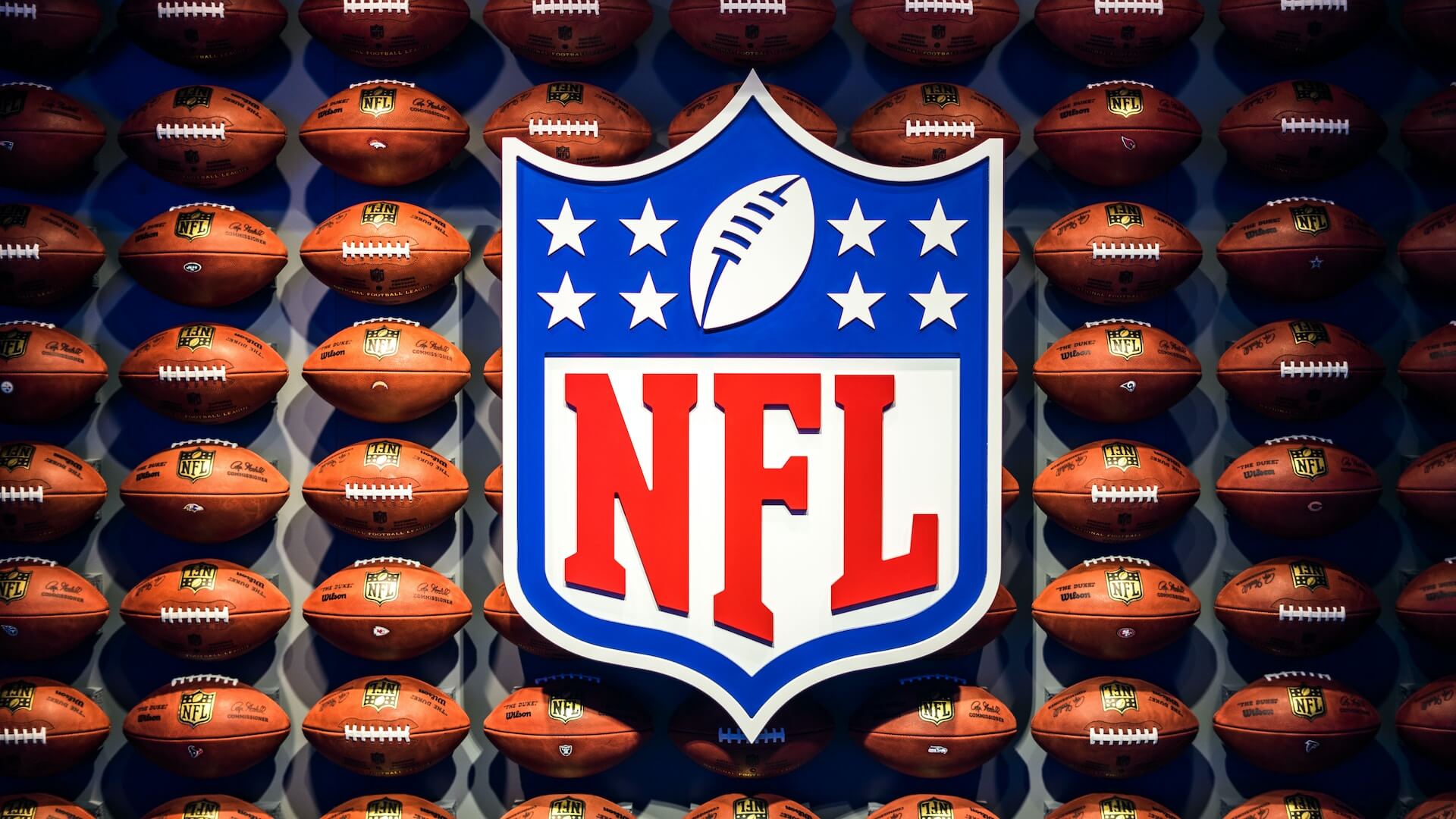 Wall full of American footballs behind large NFL logo