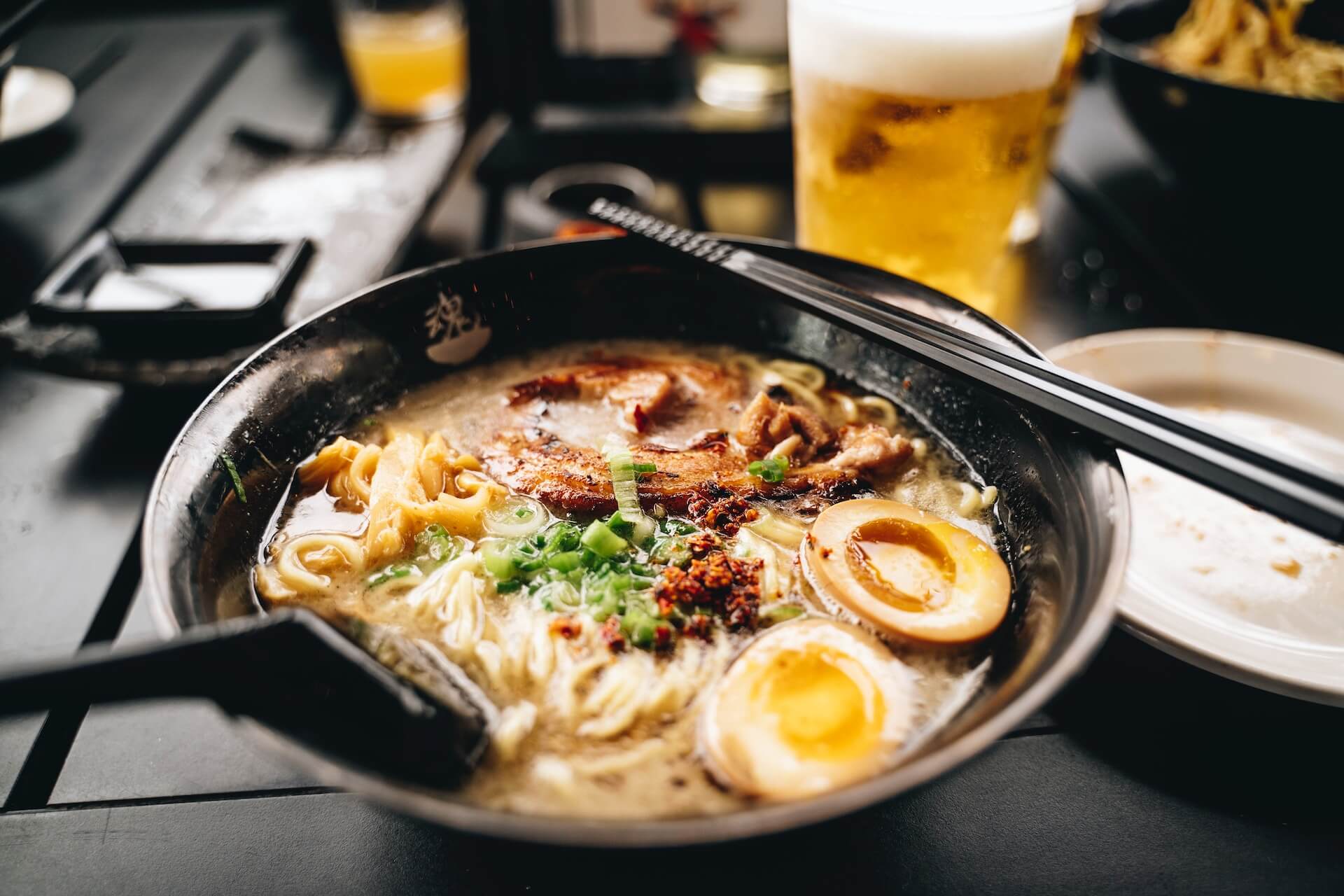 A bowl of ramen with beers in the background