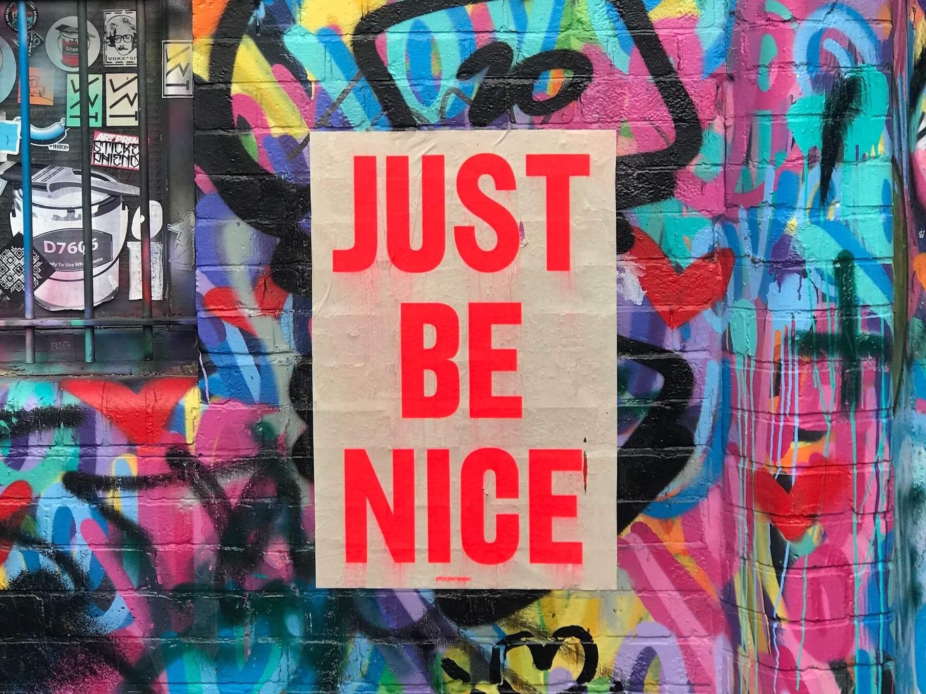 "Just be nice" sign on wall with graffiti