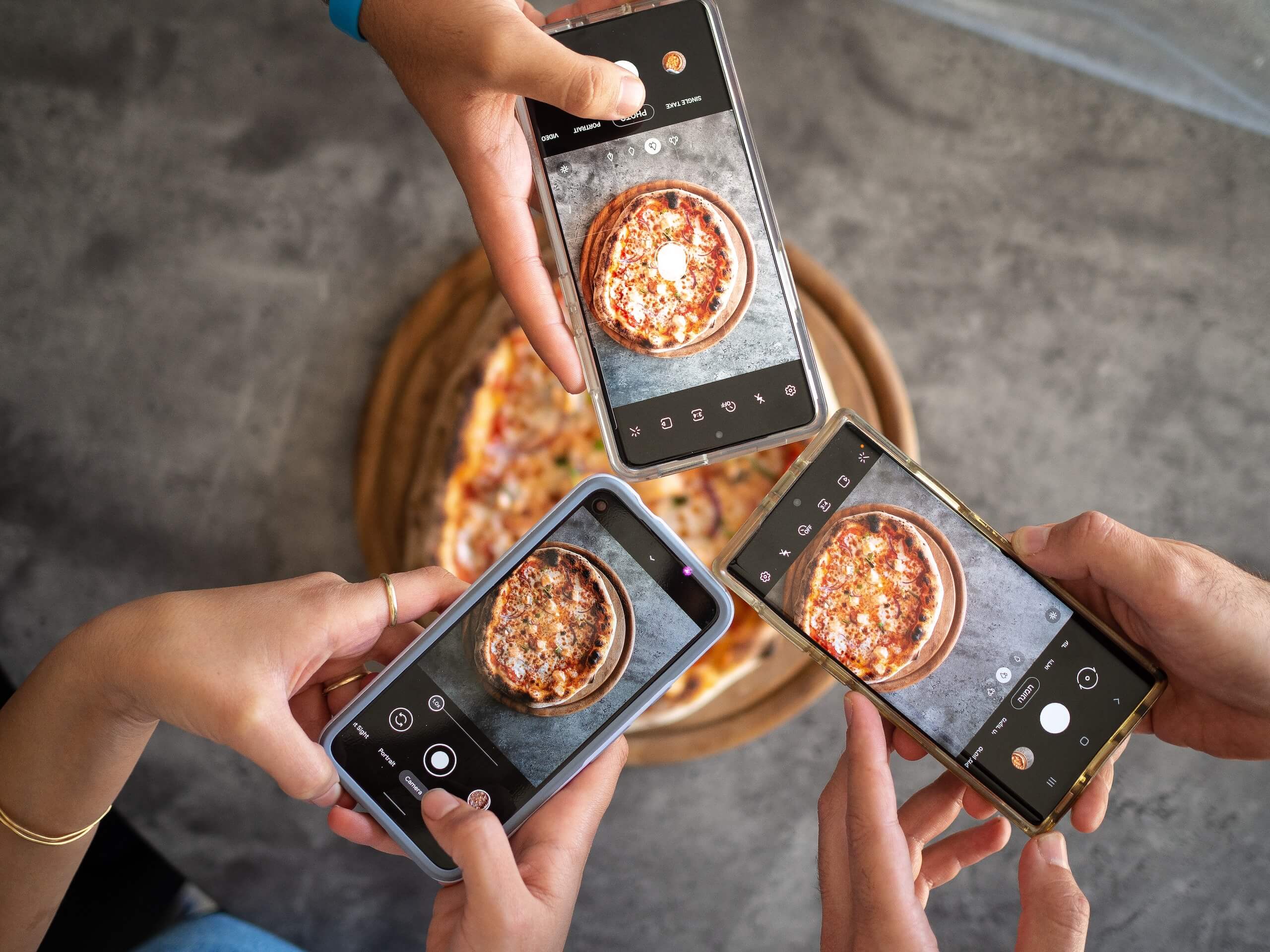 People holding phones over a pizza