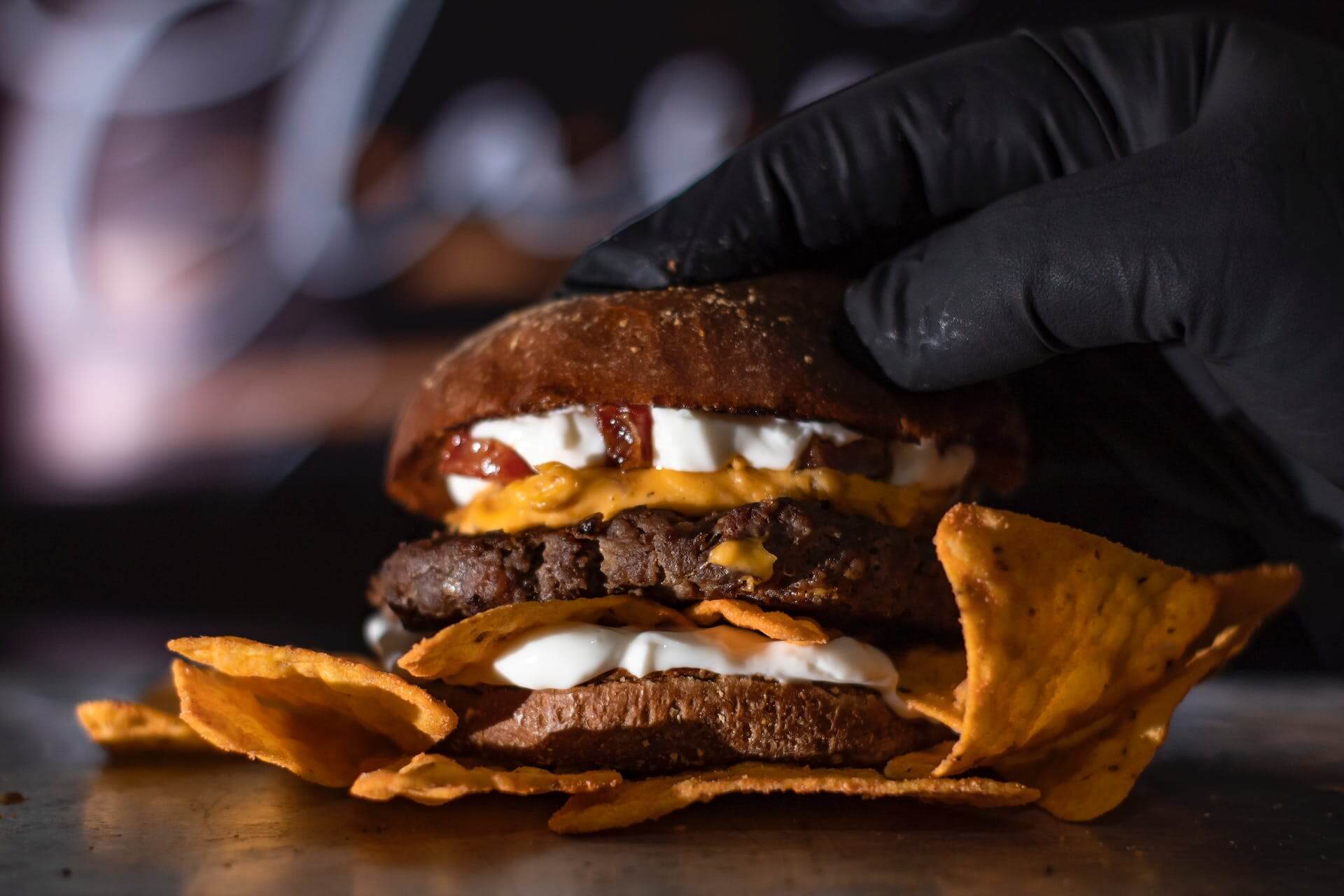 Gloved chef's hand pressing down on cheeseburger bun