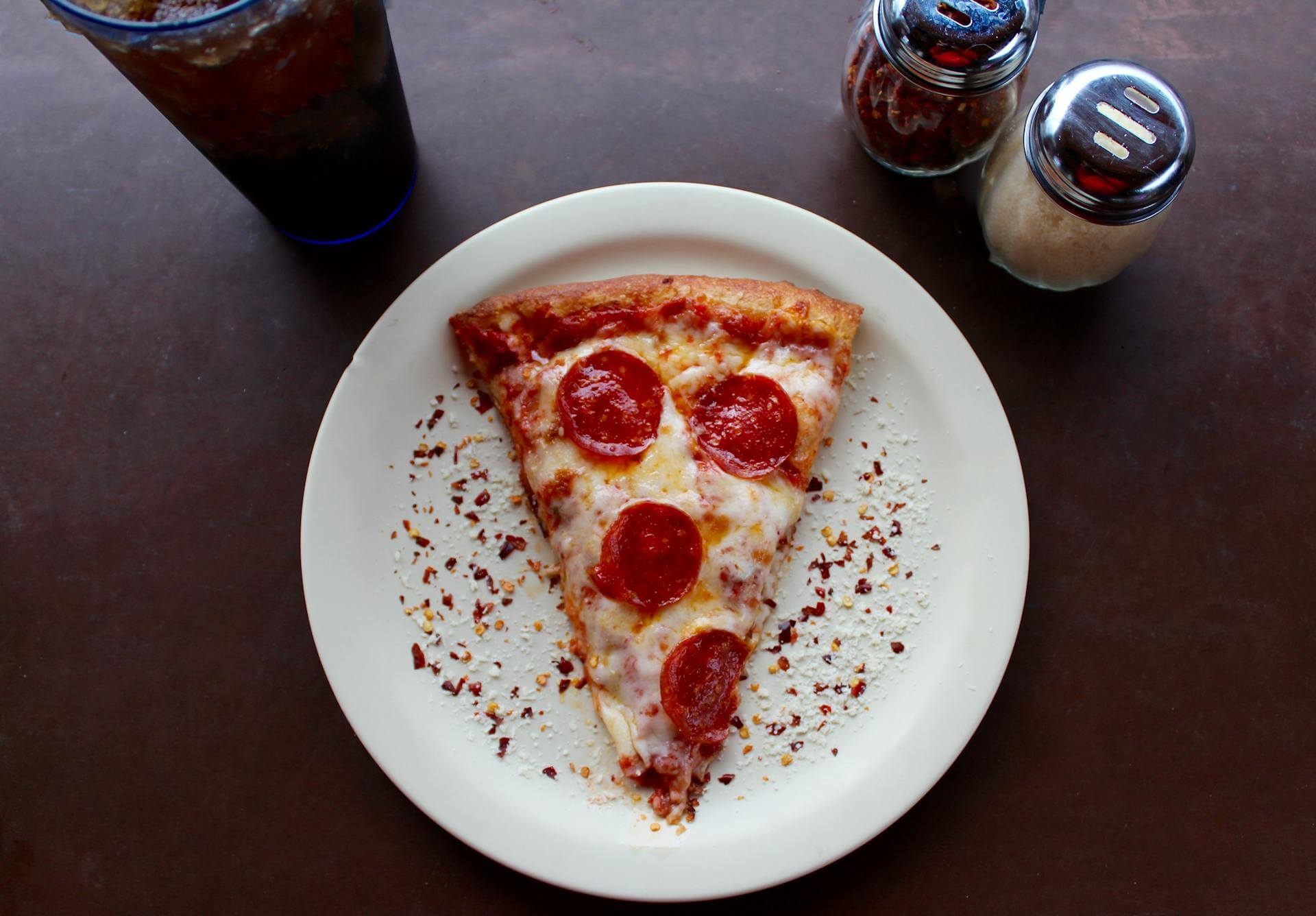 Slice of pepperoni pizza on a plate, on top of a table