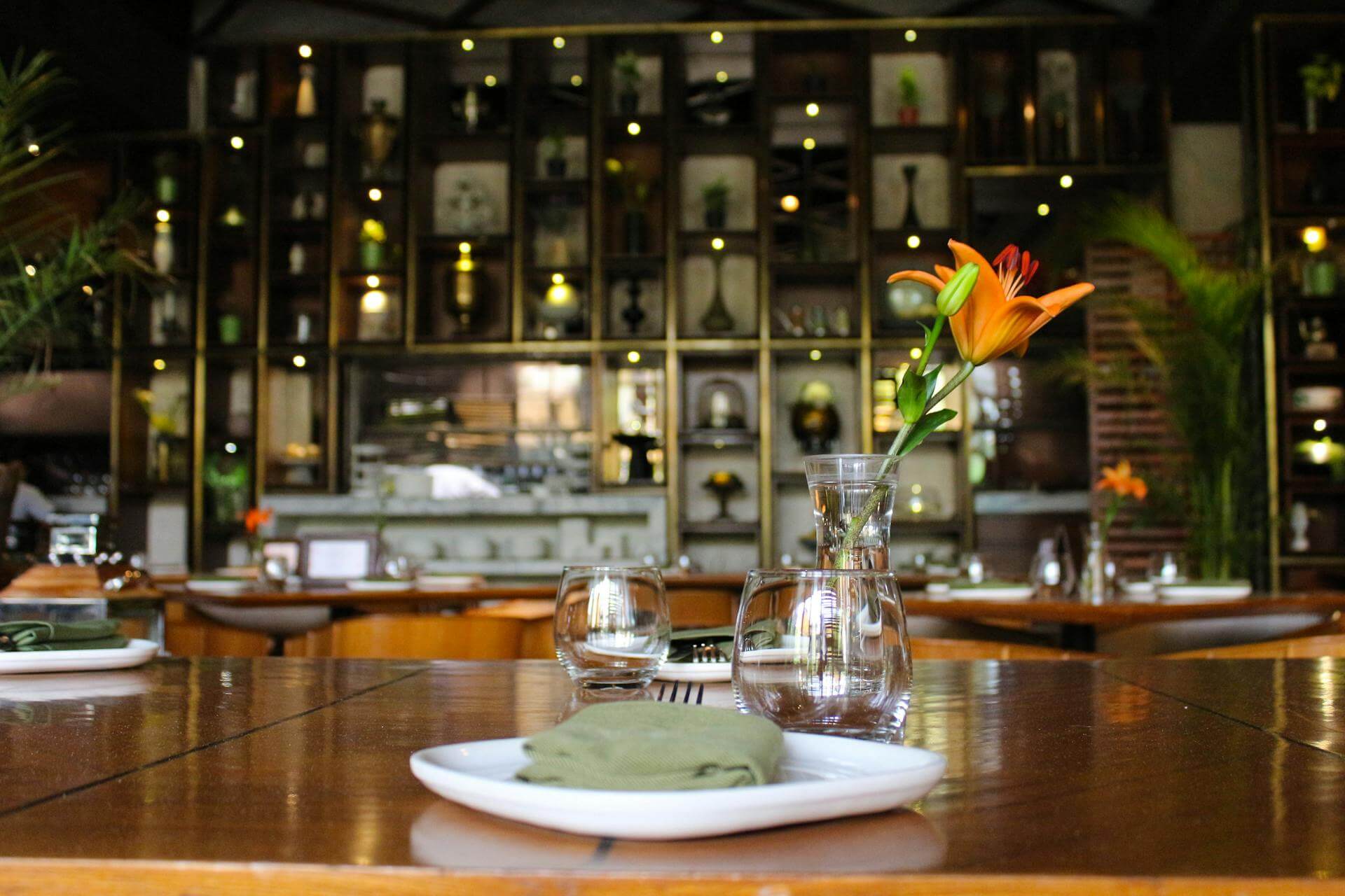 A table setting featuring white plates, green cloth napkins, and water glasses, with a vase and flower on the table