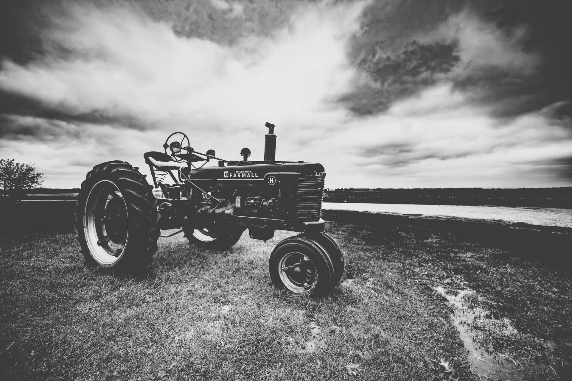 A black-and-white image of a vintage Farmall tractor in a field on a farm