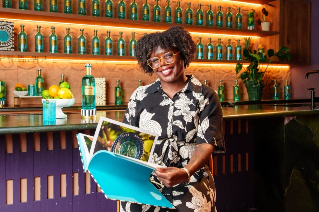 LP O'Brien, the winner of the Netflix show Drink Masters, holding an ITALICUS book, surrounded by ITALICUS bottles.