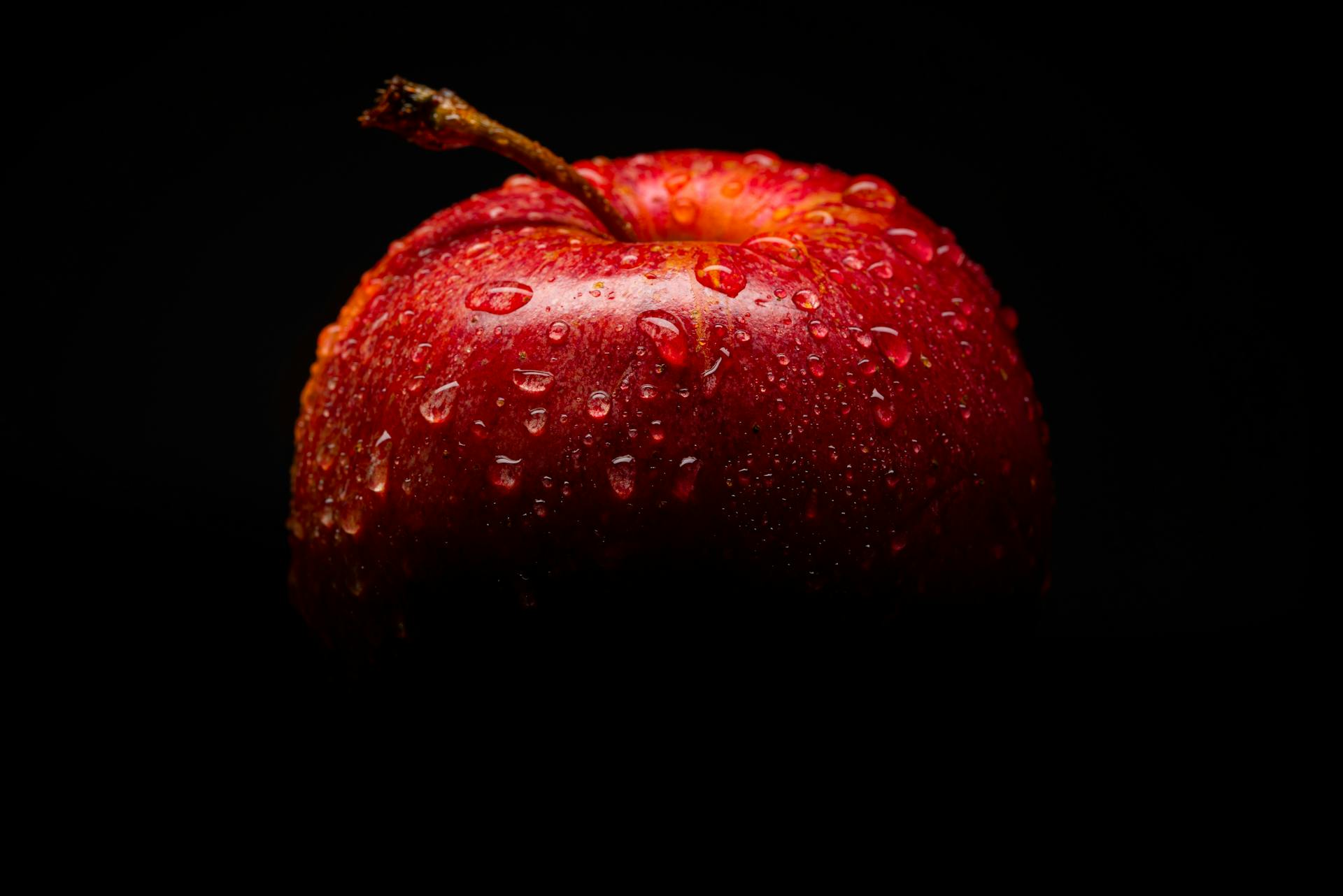 Red apple covered with water droplets, against a black background