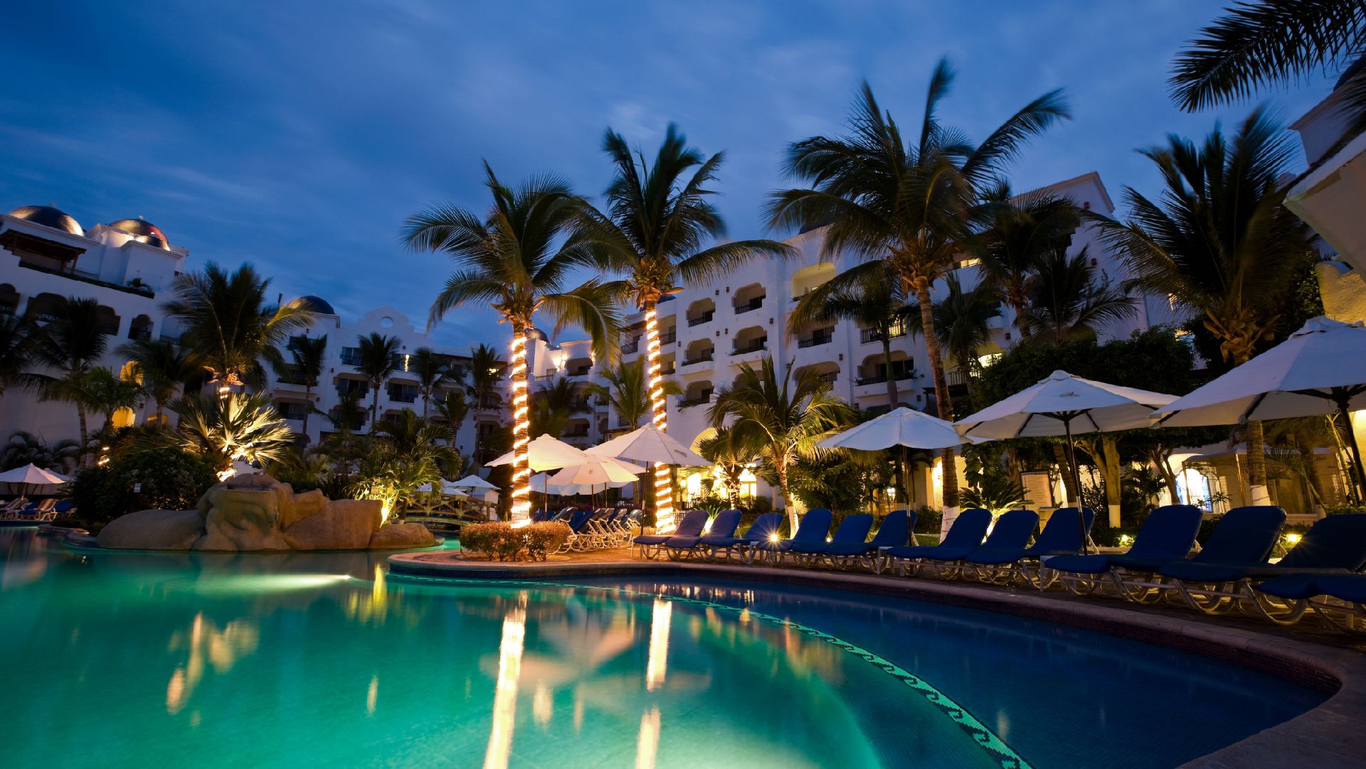 Image of a resort pool in the evening, with palm trees and the hotel in the background