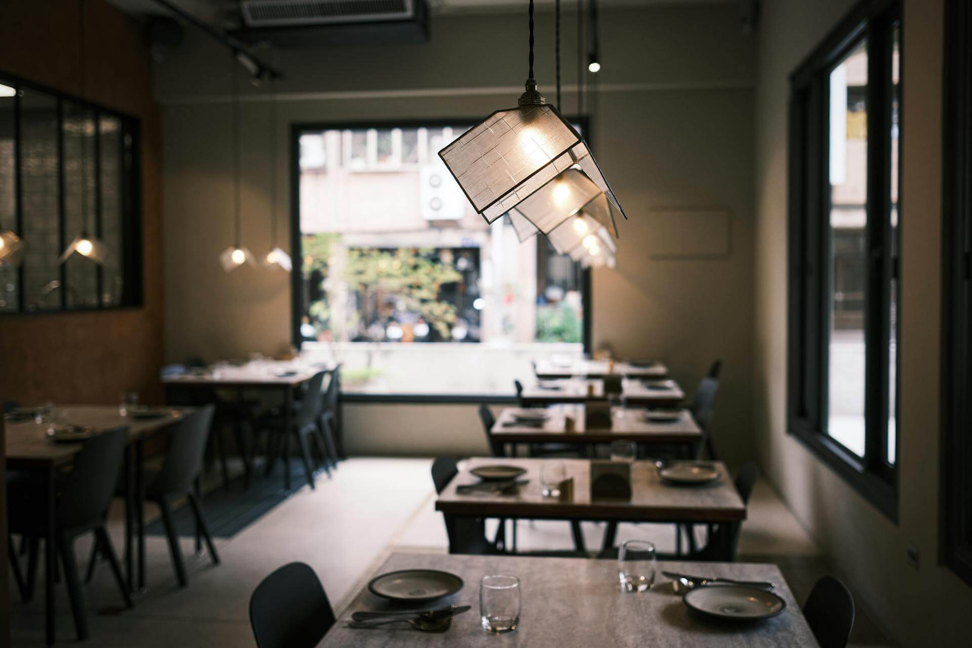 Interior of a light, relaxing restaurant with a focus on the modern, sophisticated light fixtures and open window to the sidewalk and street.