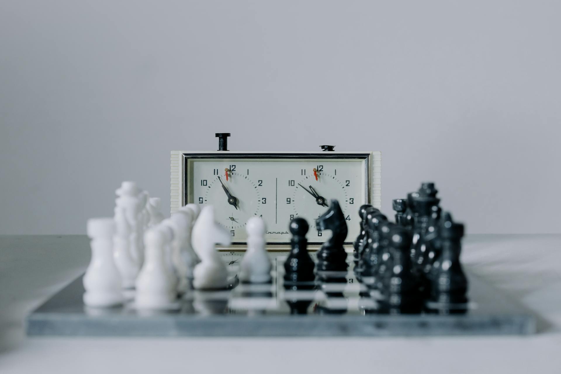 A chess clock next to a chessboard with full pieces set up