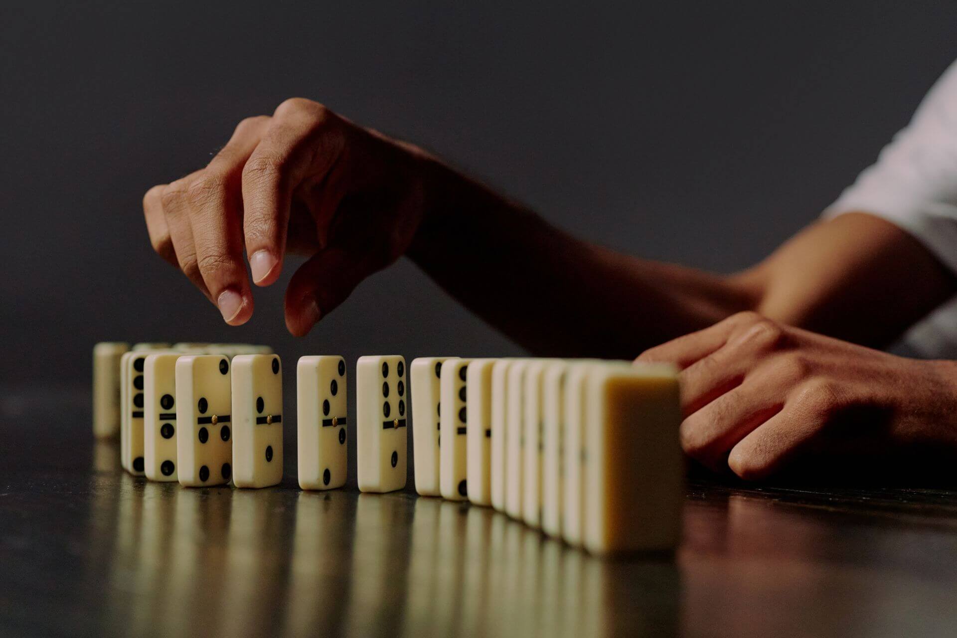 Hand carefully positioning dominoes in sequence on a table, representing the importance of building a business in the right order.